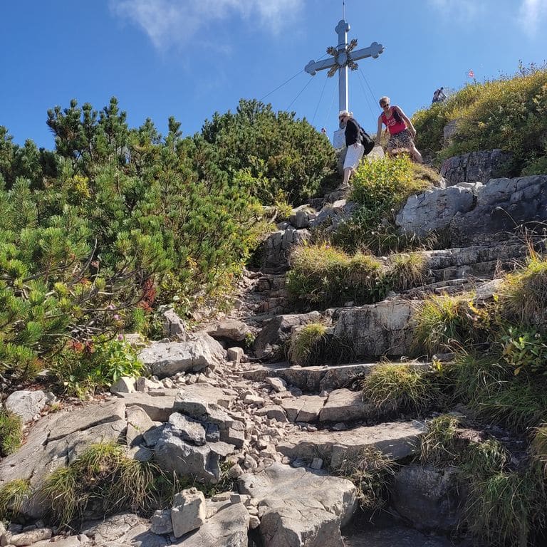 Steinstufen führen einen Berg hinauf zu einem Gipfelkreuz