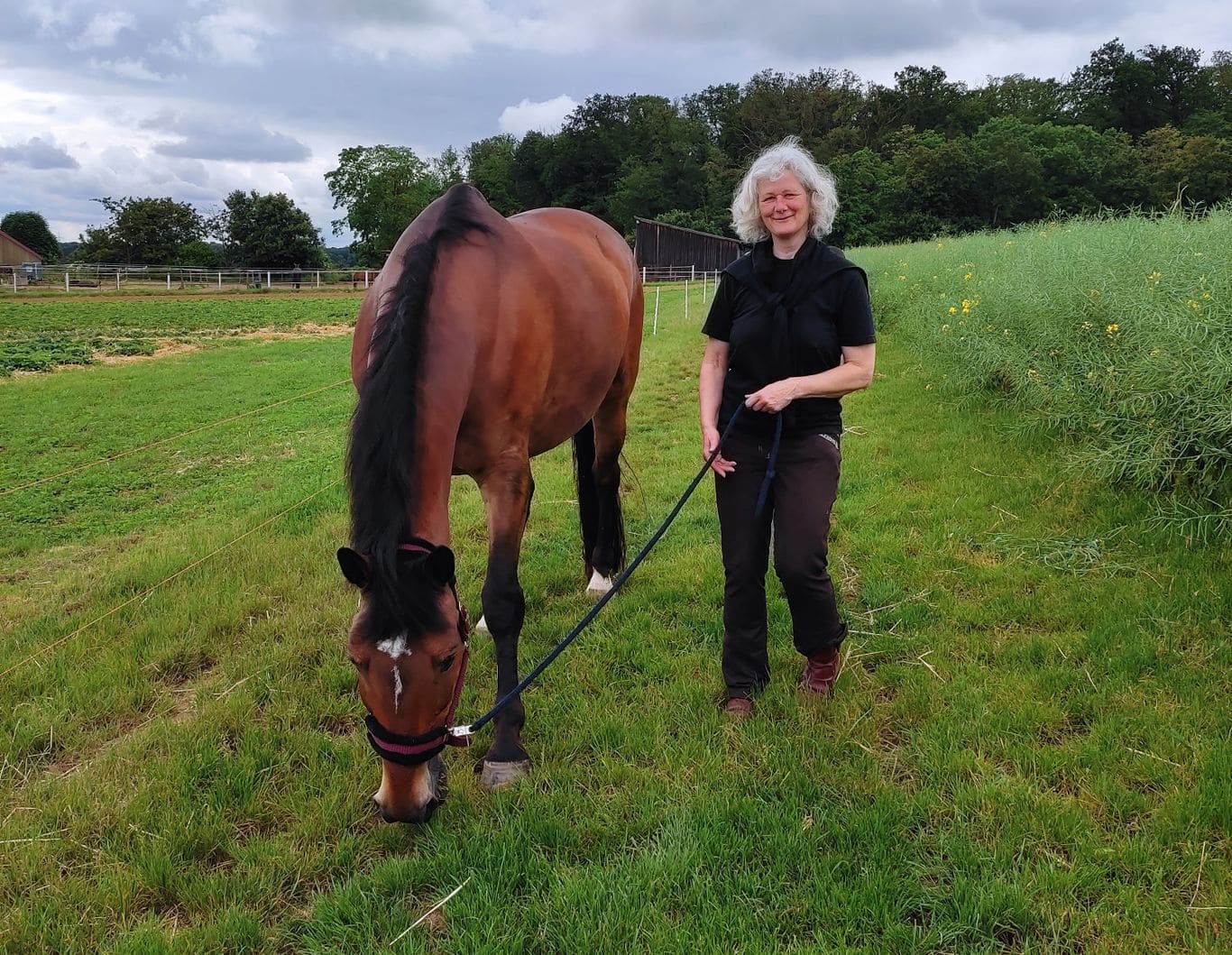 Ute Marth steht mit einem grasenden Pferd auf einer Wiese